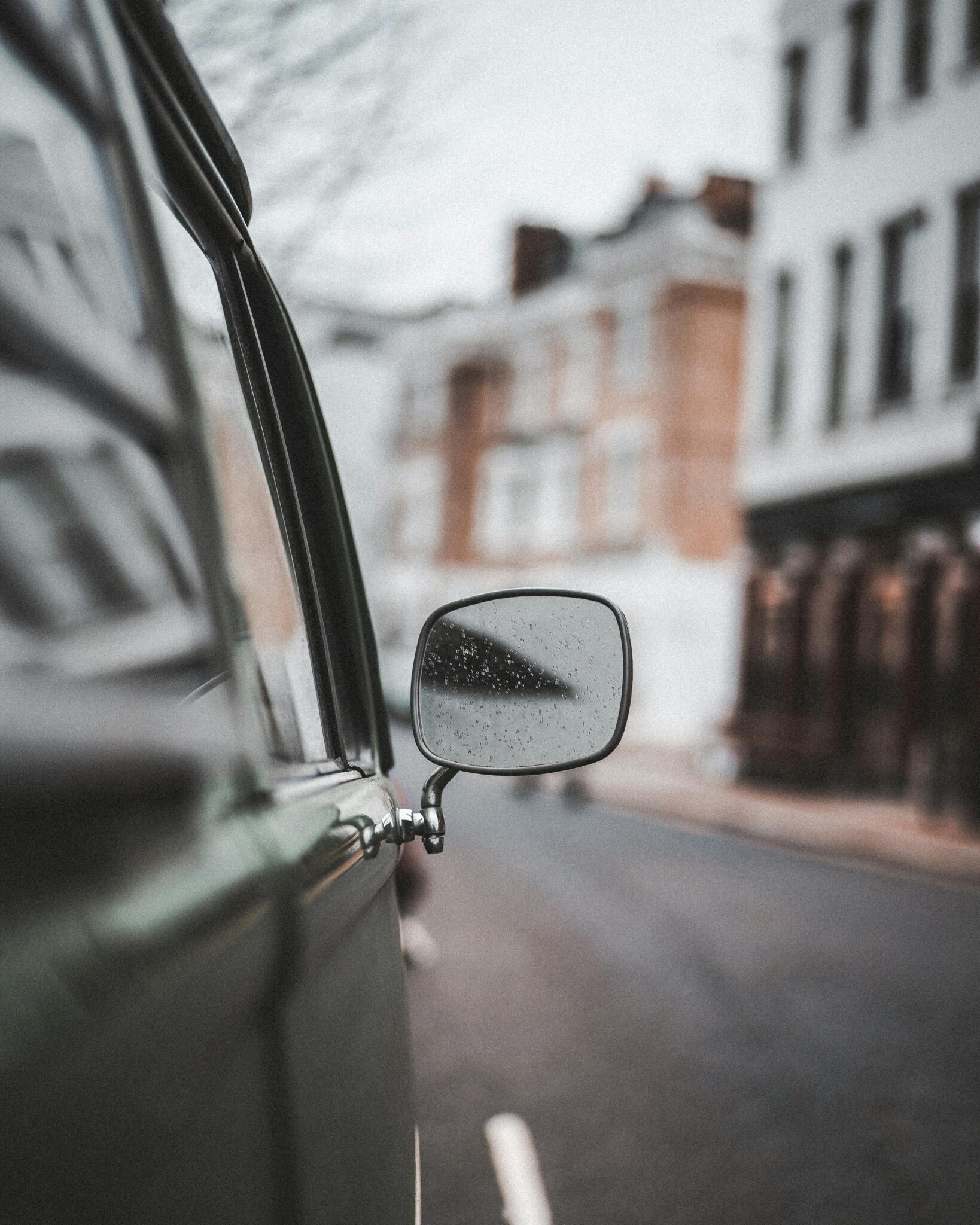 Close-up of a vintage van side mirror reflecting a blurred urban street scene.